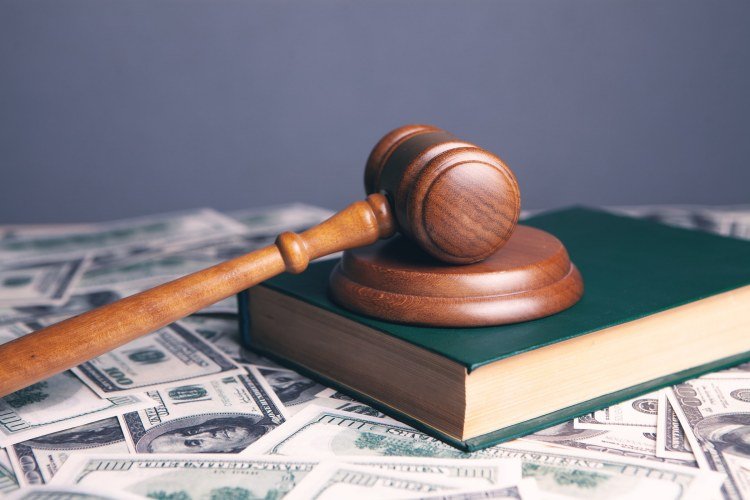 Wooden gavel and block and green hardcover book on surface covered in hundred dollar bills