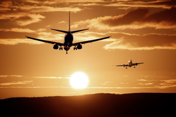 Two planes flying through cloudy orange sky at sunset