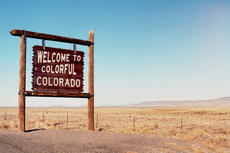 'Welcome to Colorful Colorado' on wooden sign near Rocky Mountain landscape at Colorado state border