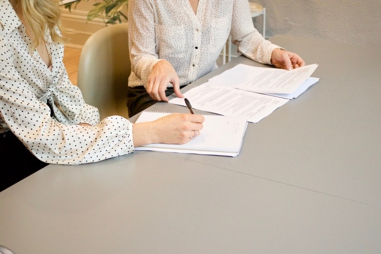 Two professionally dressed women reviewing forms in adjacent seats at table