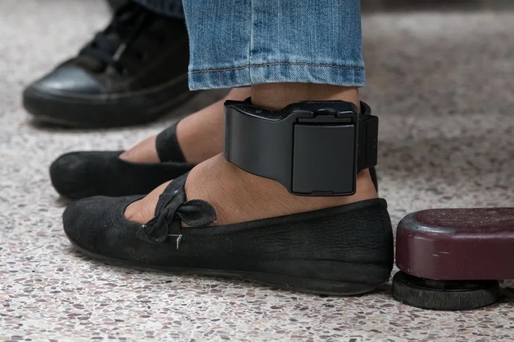 Ankle monitor device, jeans and black shoes on leg of woman indoors
