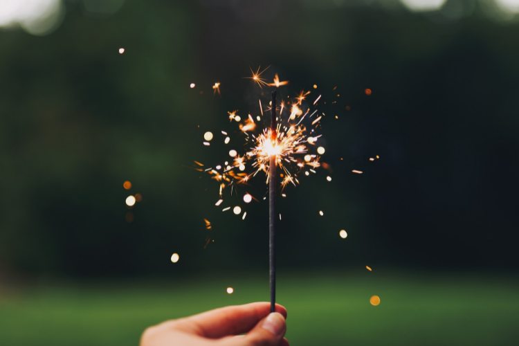 Hand holding lit sparkler in grassy, sunlit outdoor space