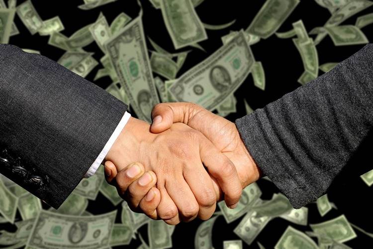 Close-up of handshake between men in business suits with dollar bills falling in background